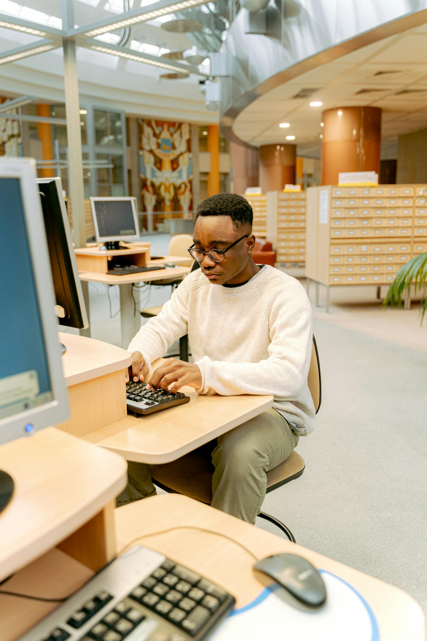 A man in a library typing on a computer, ideal for education and technology themes.