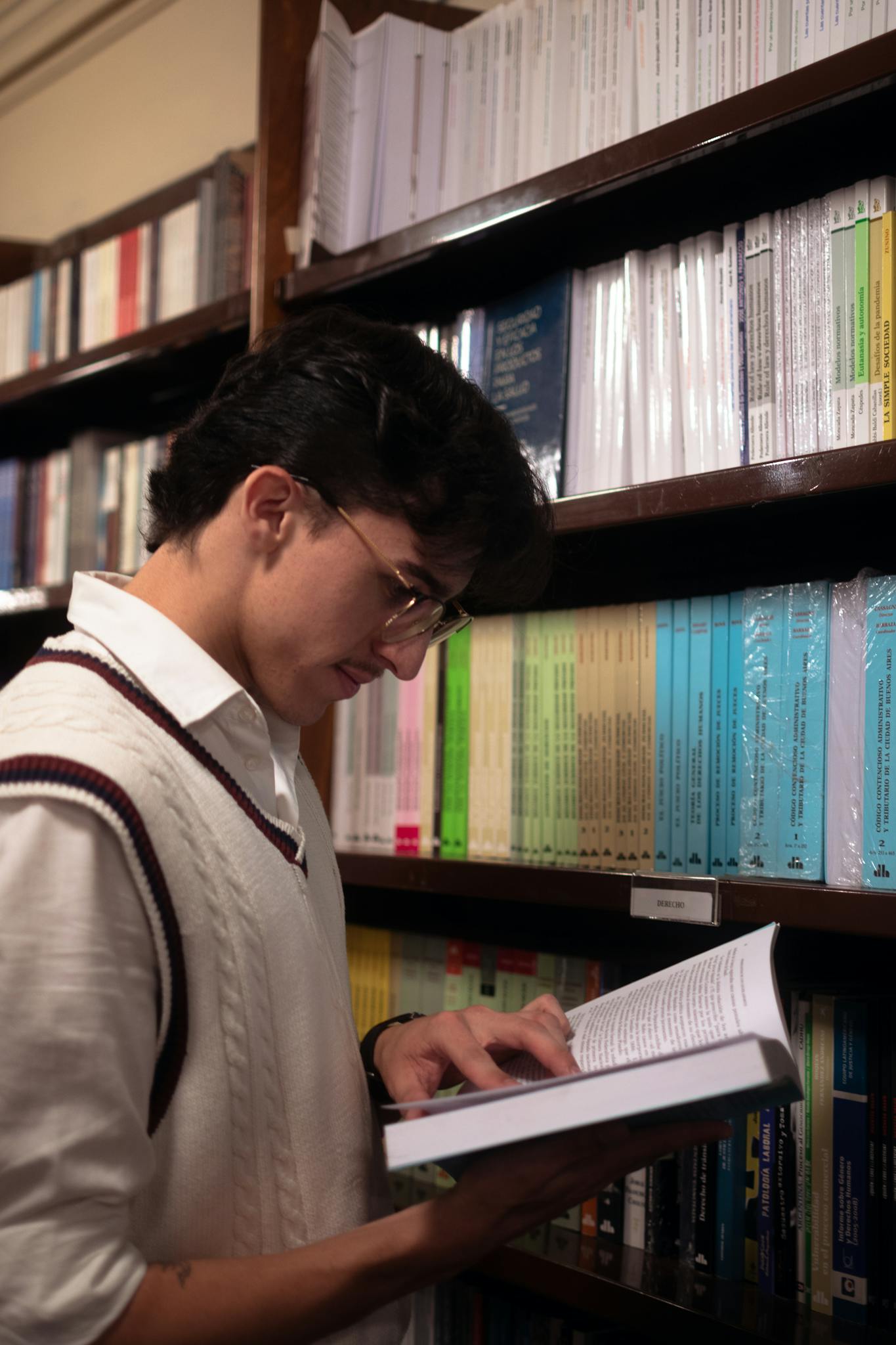 Stylish young man reading in an elegant library setting, surrounded by books.
